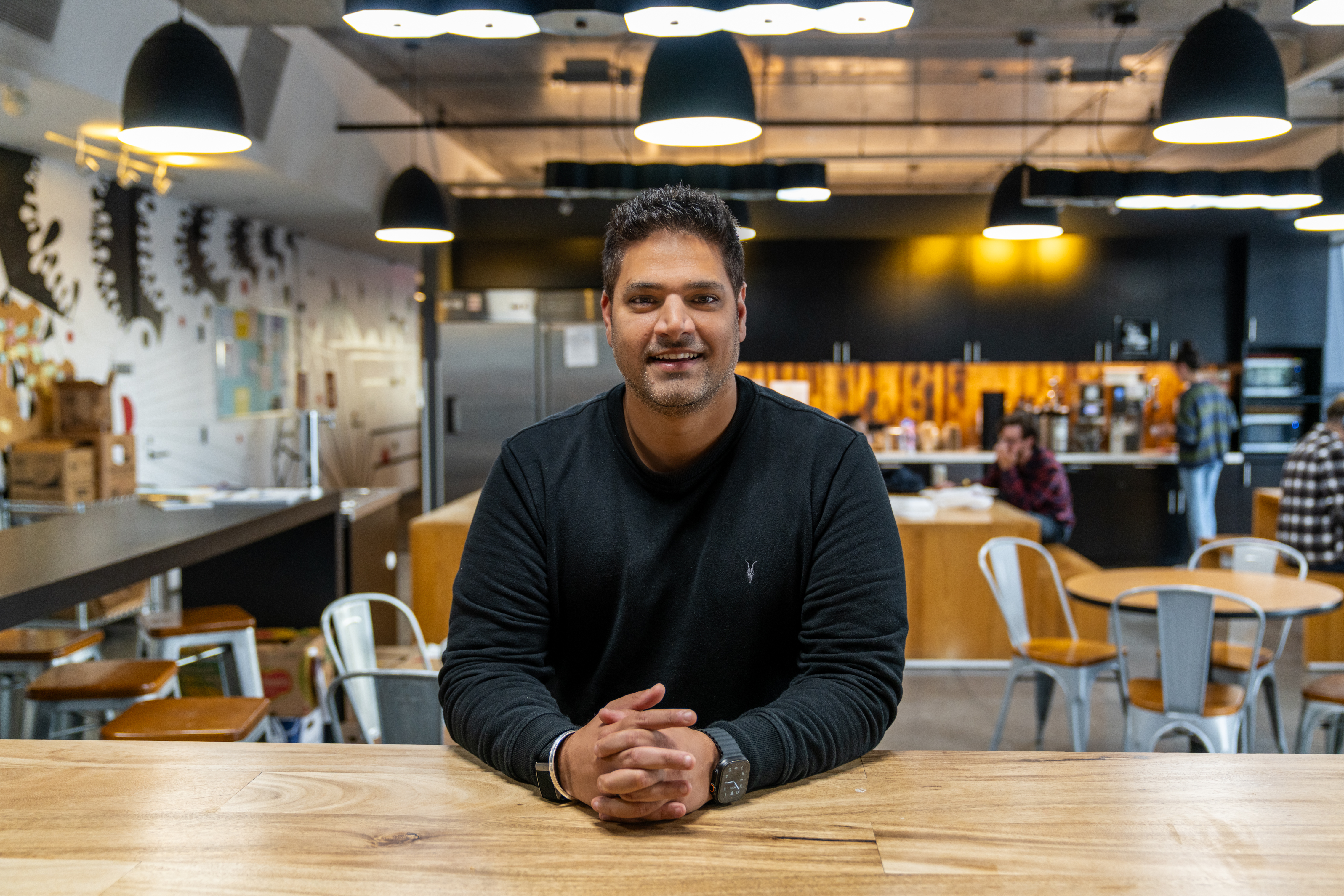 Siddharth Astir smiling, seated at a table in a workspace